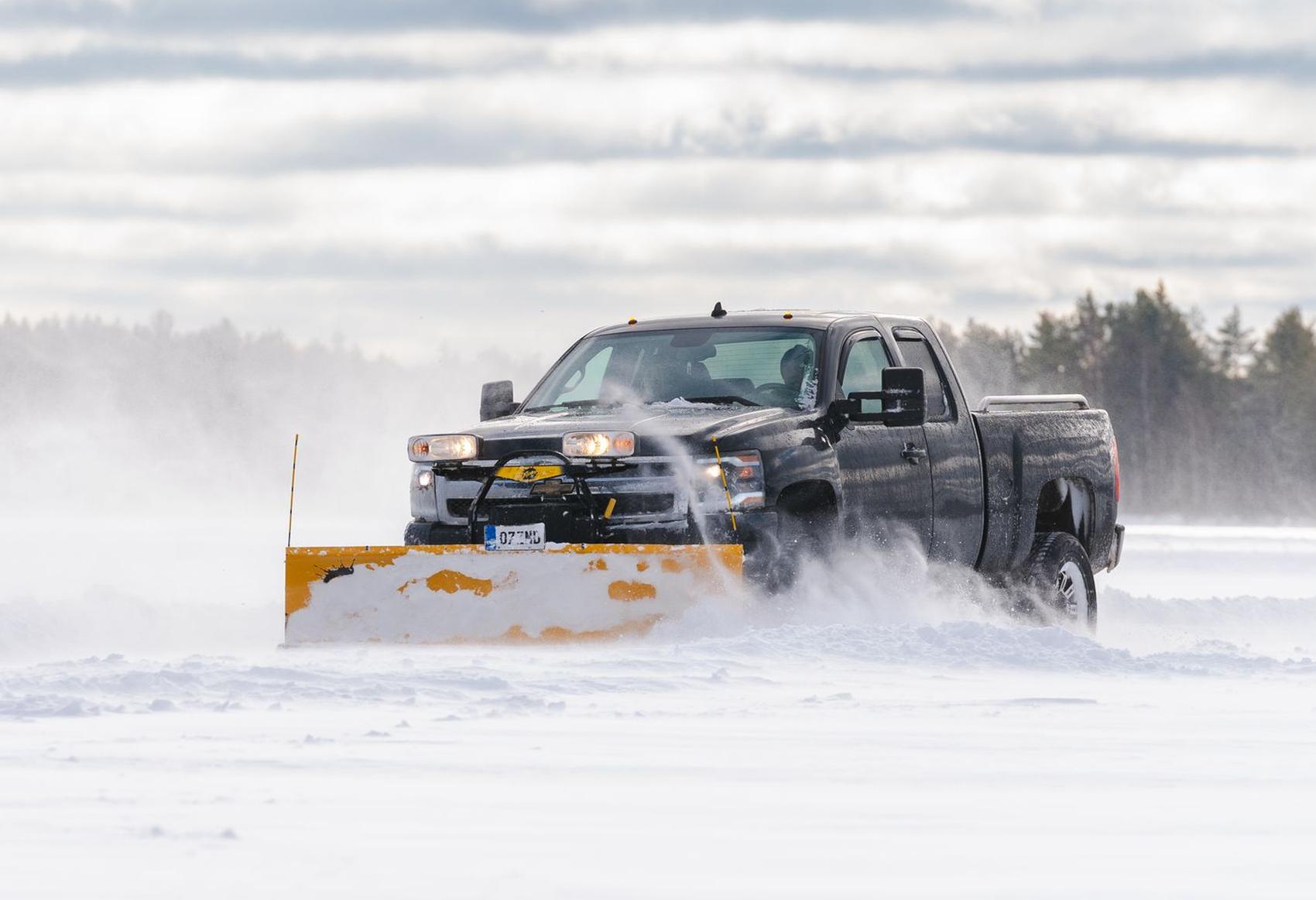 A pickup truck with a plow blade pushing snow off a road in winter.