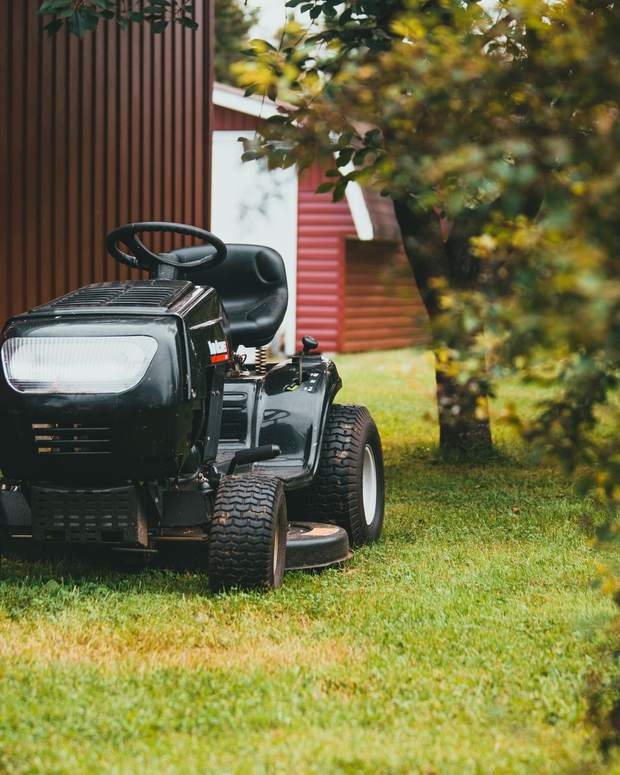 A riding mower parked on cut grass beside a red barn.