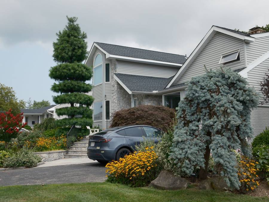A well-kept house with mature shrubs, evergreens and flower beds along the drive.